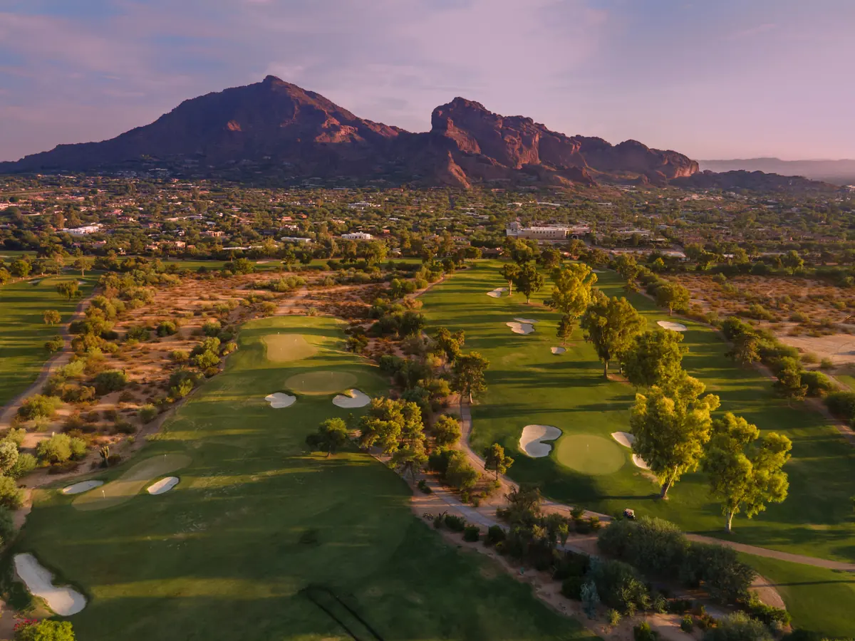 Aerial view of a manicured golf course at dusk with Camelback Mountain rising behind it
