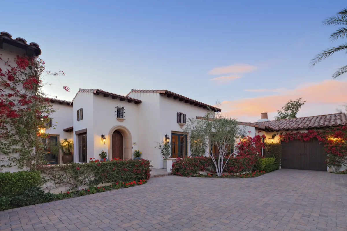 Front exterior of a white Spanish-style luxury home with a terracotta tile roof and desert landscaping