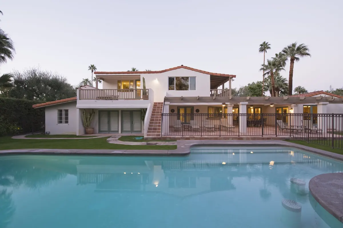 White Spanish-style home with a lit swimming pool and palm trees at dusk